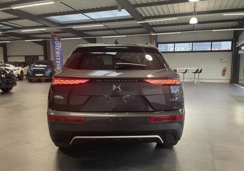 Vue arrière du DS7 Crossback gris titanium avec feux arrière LED 3D et logo DS Automobiles lumineux dans un showroom.