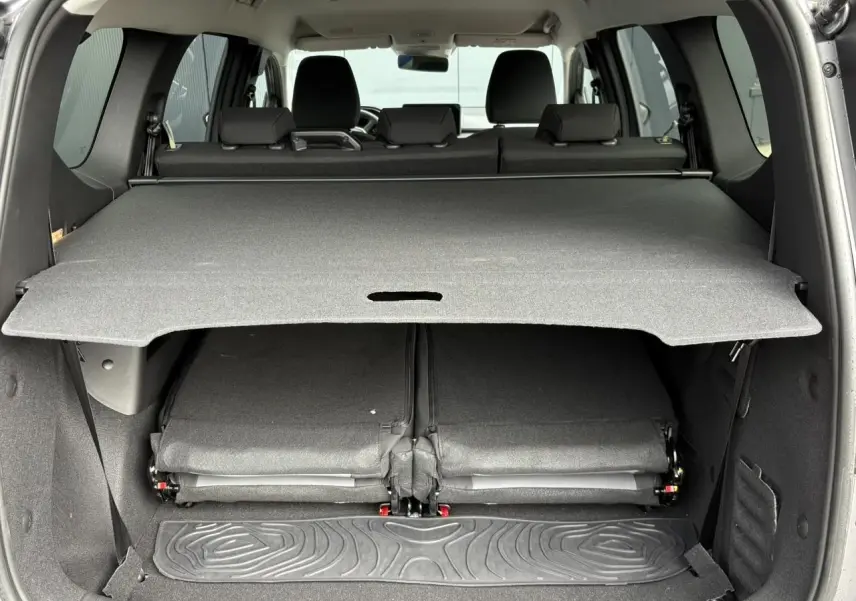 Coffre ouvert vu de l'arrière du Dacia Jogger gris Schiste avec sièges rabattus et cache-bagages déployé.