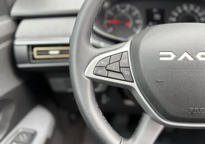 Gros plan sur le volant noir du Dacia Jogger 2025 avec commandes de régulateur de vitesse et logo central visible.