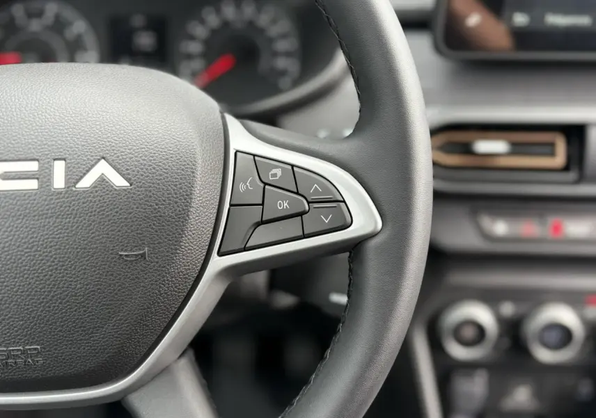 Gros plan sur le volant noir de la Dacia Jogger 2025 avec commandes intégrées et tableau de bord flou en arrière-plan.