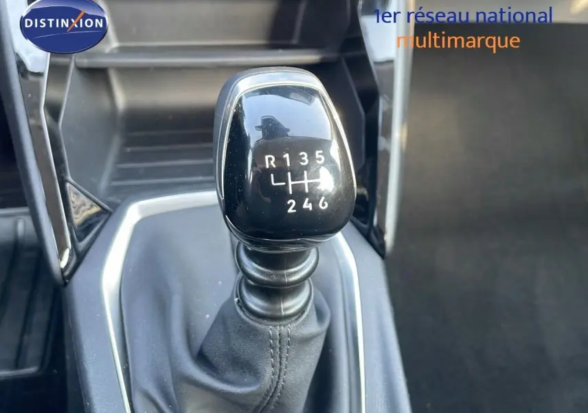 Gros plan sur le levier de vitesses manuel noir de la Peugeot 208 blanche, montrant la grille des 6 rapports et la marche arrière.