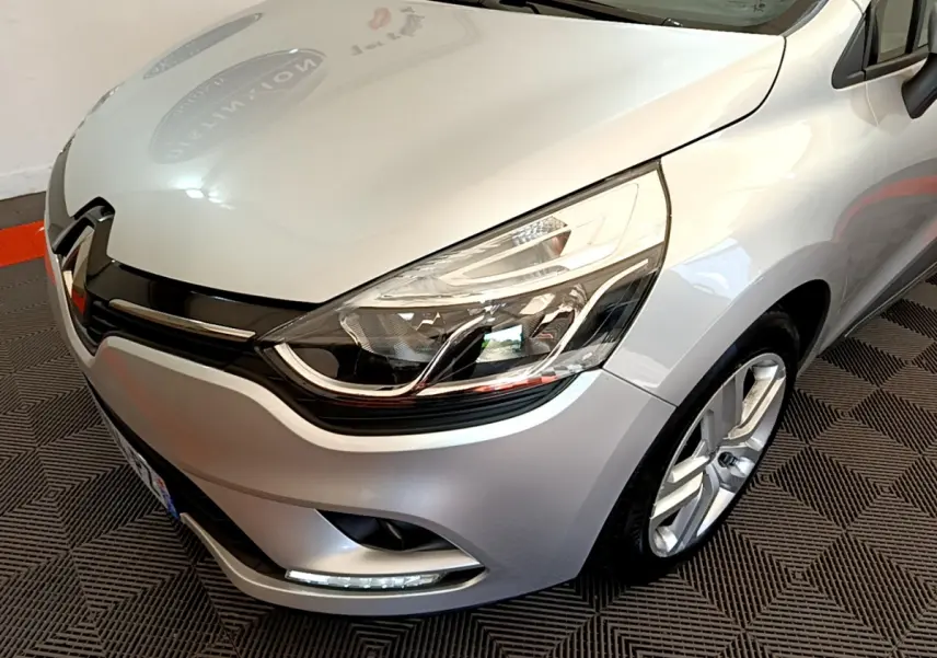 Vue 3/4 avant droit d'une Renault Clio Business TCe 90 gris clair mettant en valeur son phare LED et sa calandre chromée.