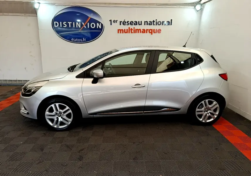 Profil côté gauche d'une Renault Clio Business TCe 90 gris clair, en intérieur avec logo Distinxion en arrière-plan.