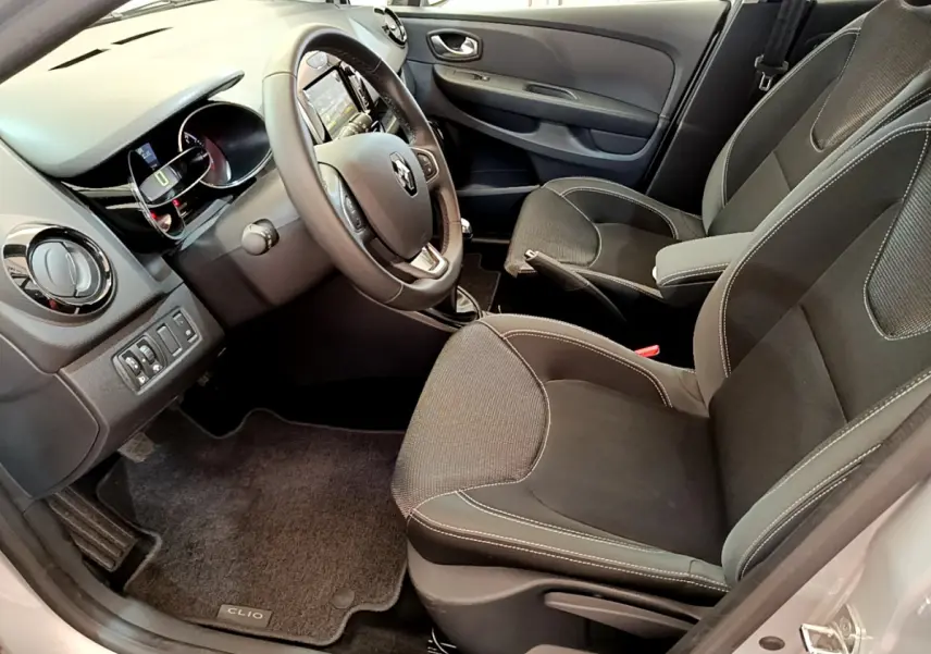 Vue intérieure côté conducteur de la Renault Clio Business TCe 90 2019 avec sièges noirs et volant cuir multifonctions.