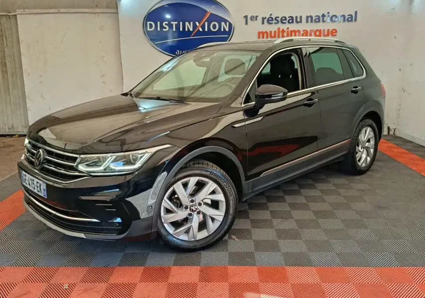 Volkswagen Tiguan noir vu en 3/4 avant droit dans un showroom avec sol à damier gris et rouge.