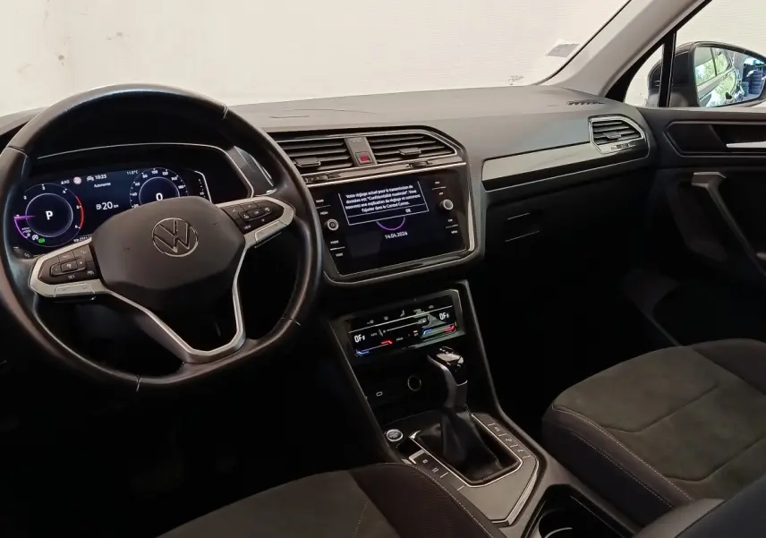 Vue intérieure avant du Volkswagen Tiguan noir 2022, tableau de bord digital et écran tactile central visibles.