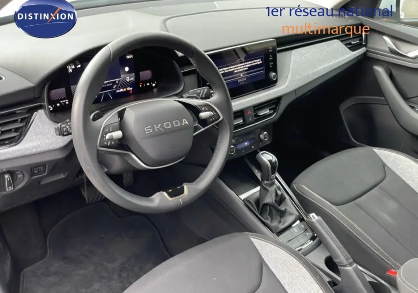 Vue intérieure avant du Skoda Kamiq blanc glacier, mettant en valeur le volant multifonction et la console centrale avec boîte automatique.