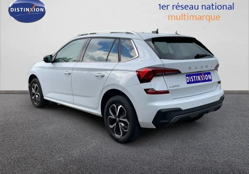 Vue 3/4 arrière droite d'un Skoda Kamiq blanc glacier avec jantes noires et toit équipé de barres de toit.