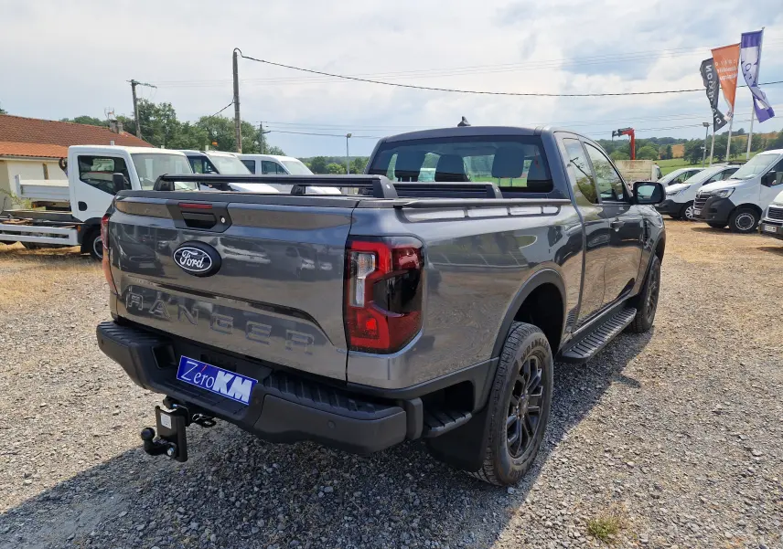 Ford Ranger Super Cabine gris carbone vu en 3/4 arrière droit, avec rideau de plateau rigide et barres de toit visibles.