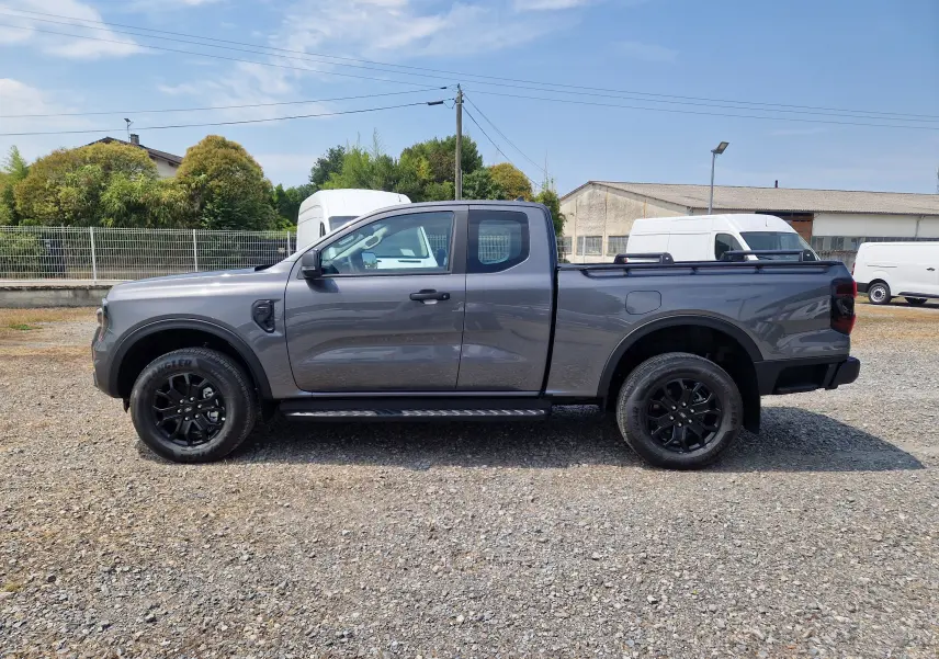 Vue de profil côté gauche du Ford Ranger Super Cabine gris carbone avec marchepied et barres sur le plateau.