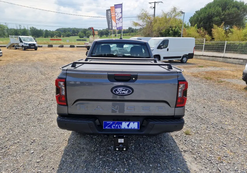 Vue arrière d'un Ford Ranger Super Cabine gris carbone avec rideau de plateau rigide et attelage visible.