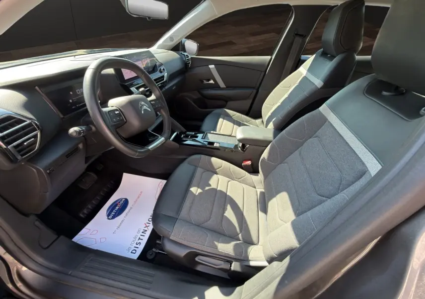 Vue intérieure côté conducteur de la Citroën C4 2023 gris foncé, volant cuir multifonctions et sièges tissu-cuir bicolores.