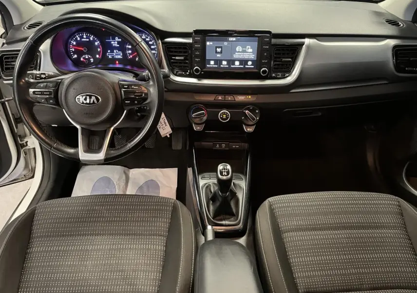 Vue intérieure avant du Kia Stonic blanc 2019, volant cuir, tableau de bord avec écran tactile 7 pouces et levier de vitesse manuel.