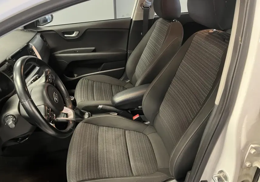 Vue intérieure côté conducteur du Kia Stonic blanc 2019, sièges tissu noir Austin avec volant cuir et console centrale.