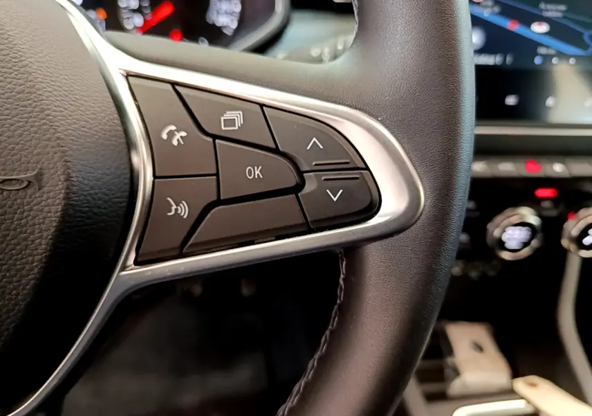 Gros plan sur les commandes du volant en cuir synthétique de la Renault Clio Business TCe 100, tableau de bord flou en arrière-plan.