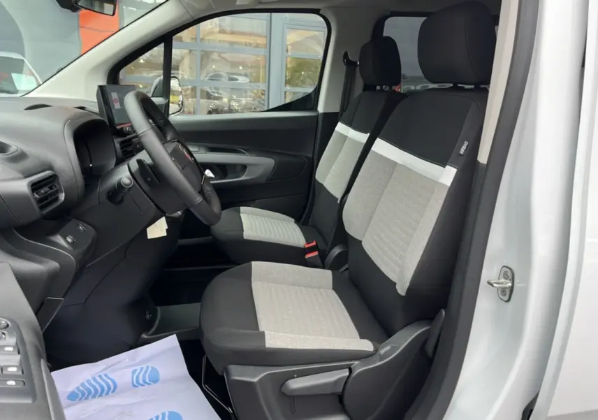 Vue intérieure côté conducteur du Citroën Berlingo blanc Kaolin, montrant les sièges tissu bicolores et le volant multifonctions.