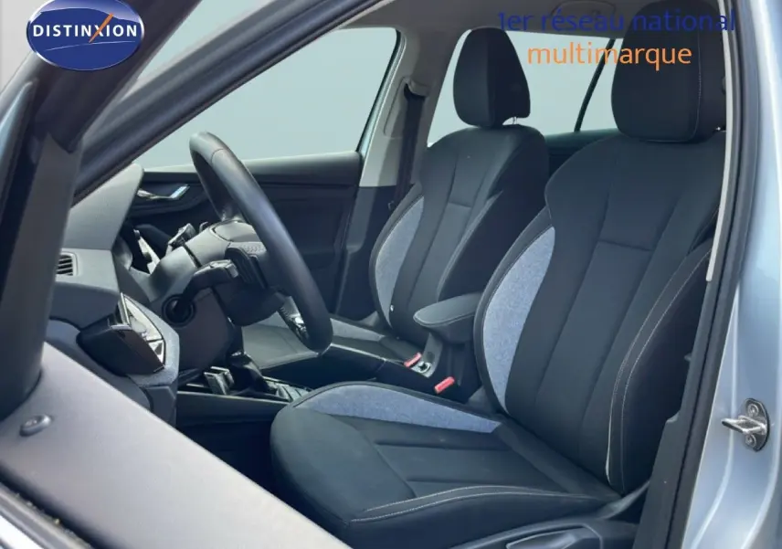 Vue intérieure côté gauche du Skoda Kamiq gris argent métal 2025, mettant en valeur les sièges avant en tissu noir et gris.