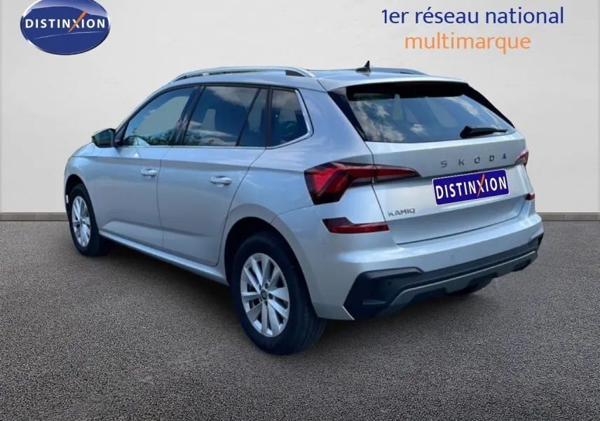 Vue 3/4 arrière droite d'un Skoda Kamiq gris argent métallisé avec feux arrière LED et toit avec barres de toit.