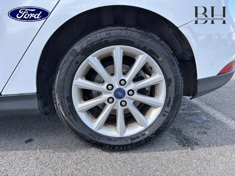 Gros plan sur la roue arrière droite de la Ford Focus blanc glacier avec jante alu et logo Ford au centre.