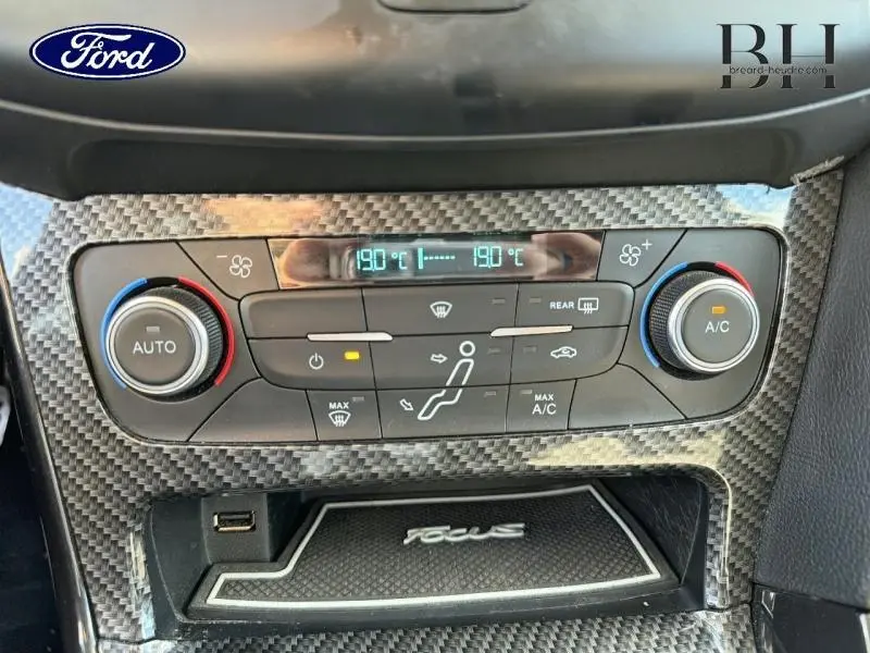 Vue rapprochée de la console centrale avec commandes climatisation et finition carbone dans une Ford Focus blanche.