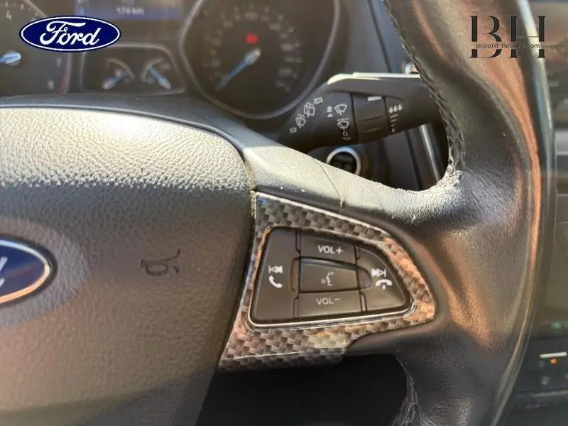 Gros plan sur le volant cuir de la Ford Focus 2016, boutons de commande audio intégrés avec finition carbone.