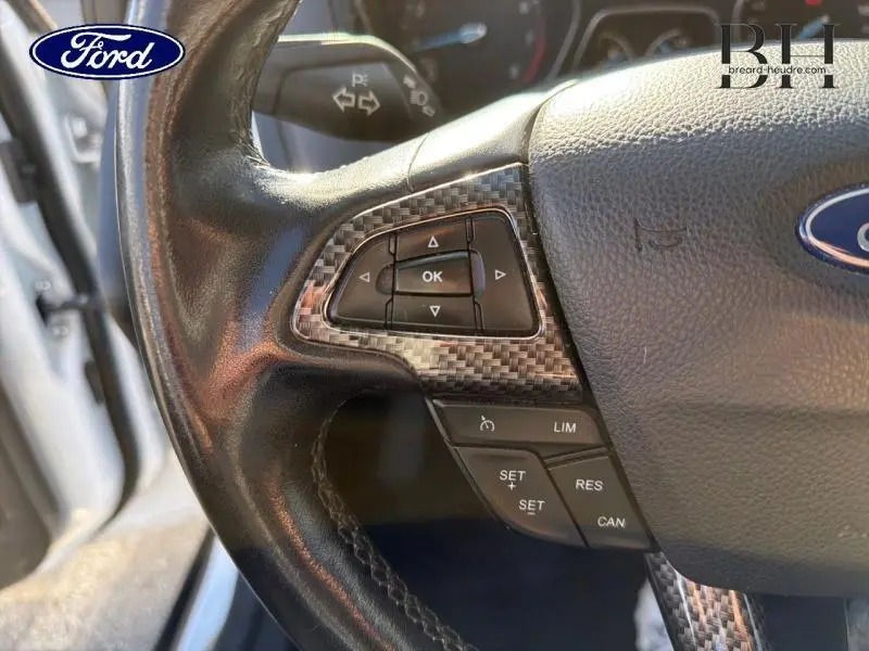 Gros plan sur la partie gauche du volant cuir multifonction de la Ford Focus blanc Glacier, avec commandes intégrées.