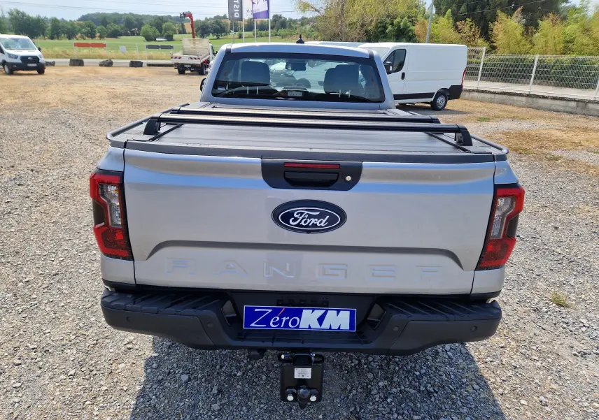 Vue arrière d'un Ford Ranger Super Cabine gris Iconic avec plateau couvert et attelage visible sur un sol gravillonné.
