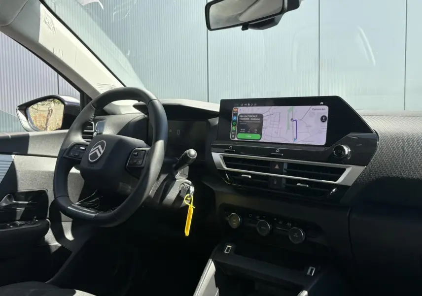 Intérieur de la Citroën C4 Hybrid 2025 vu côté conducteur, tableau de bord noir avec écran tactile de navigation allumé.