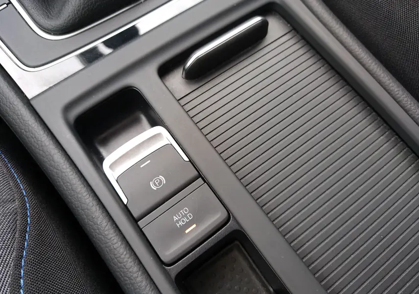 Gros plan intérieur sur la console centrale noire de la Volkswagen Golf gris reflet d'argent, avec bouton frein à main électronique et Auto Hold.