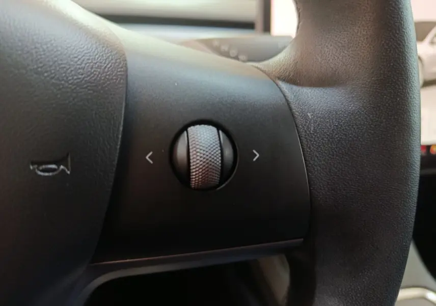 Gros plan sur la molette de commande noire du volant en cuir synthétique d'une Tesla Model 3 blanche de 2022.