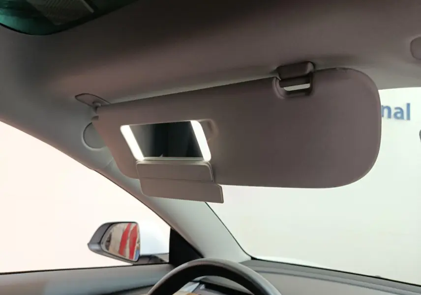 Vue intérieure côté conducteur du pare-soleil relevé avec miroir éclairé dans une Tesla Model 3 blanche 2022.