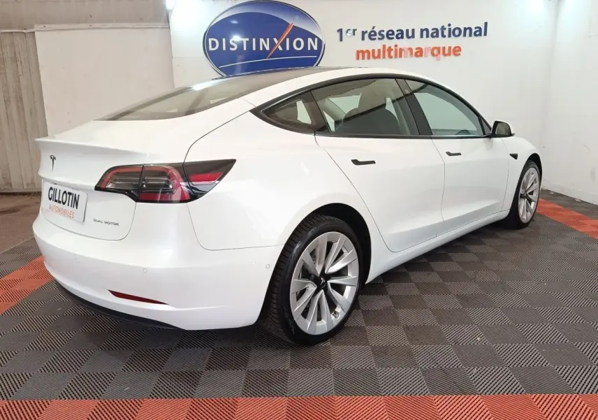 Tesla Model 3 Grande Autonomie blanc vue 3/4 arrière droit dans un showroom avec logo Distinxion en arrière-plan.