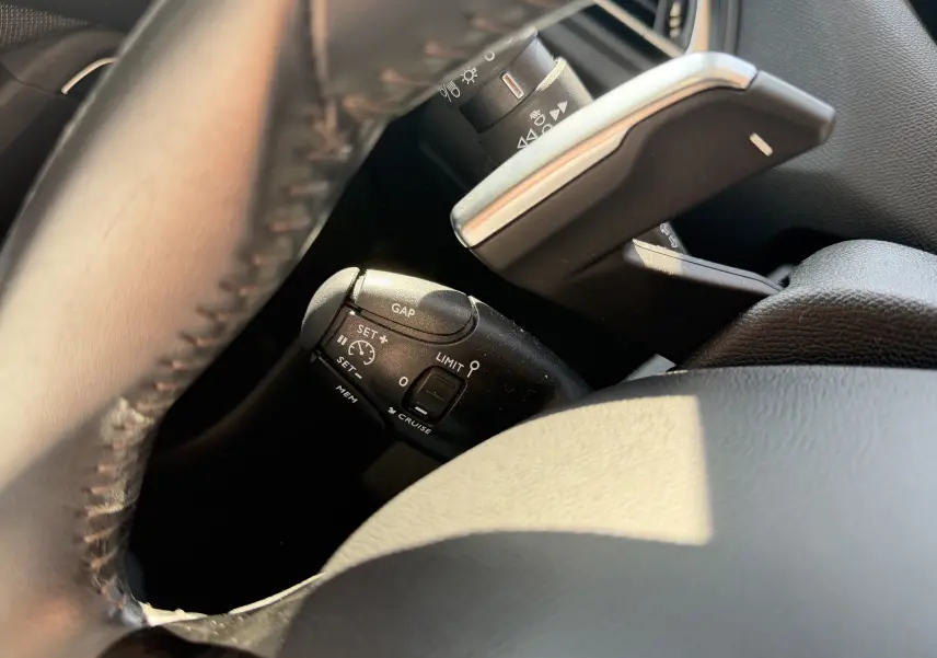 Gros plan sur les commandes de régulateur de vitesse et limiteur, près du volant noir du Peugeot 308 SW rouge rubis.