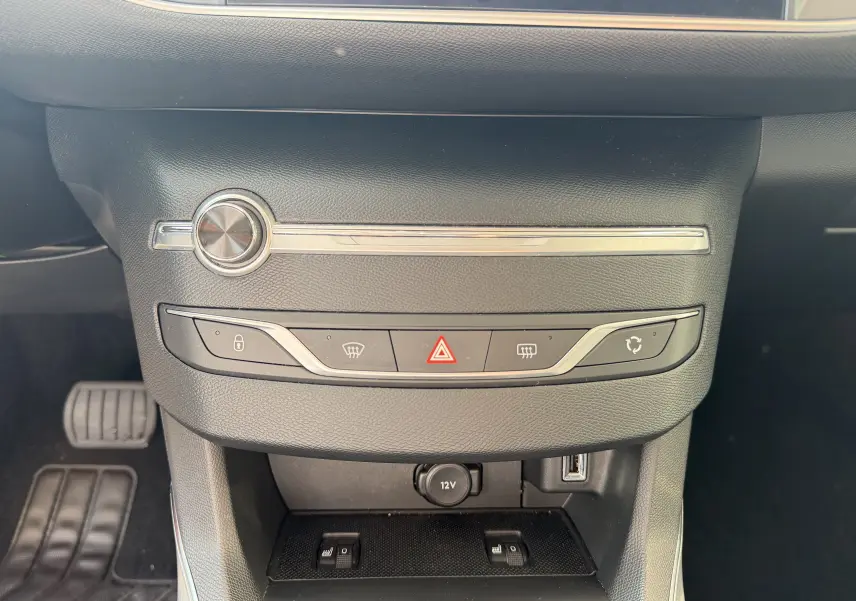 Gros plan sur la console centrale noire du Peugeot 308 SW rouge rubis, montrant les commandes de climatisation et prises USB et 12V.