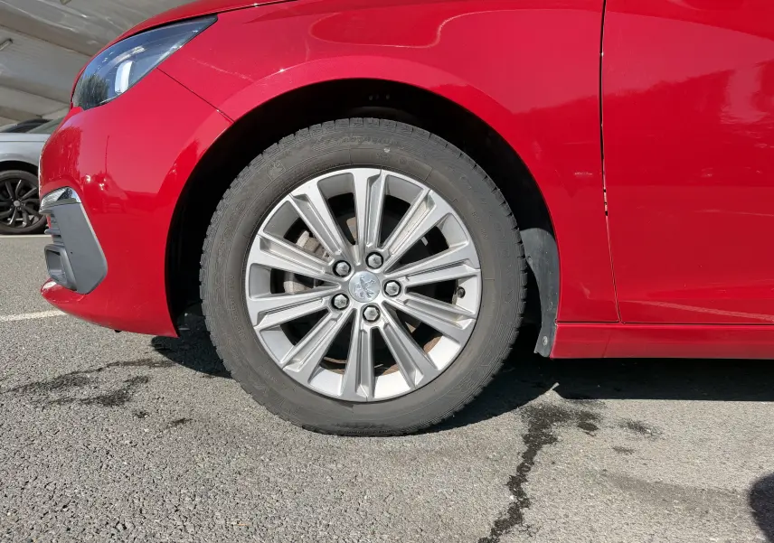 Gros plan sur la roue avant gauche d’une Peugeot 308 SW rouge rubis, avec jante alliage et partie du pare-chocs avant visible.