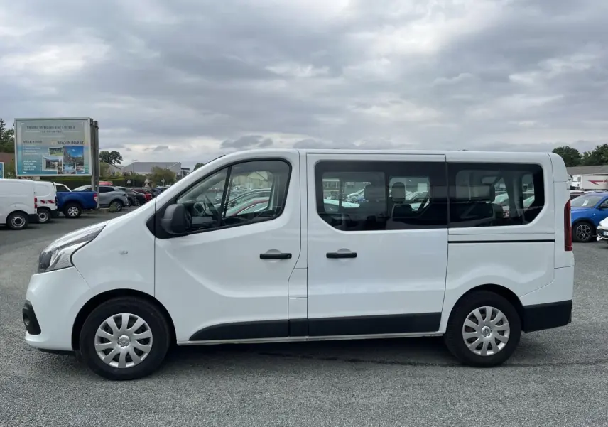 Profil côté gauche d'un Renault Trafic Fourgon blanc 2016 avec porte latérale coulissante et vitres arrière vitrées.