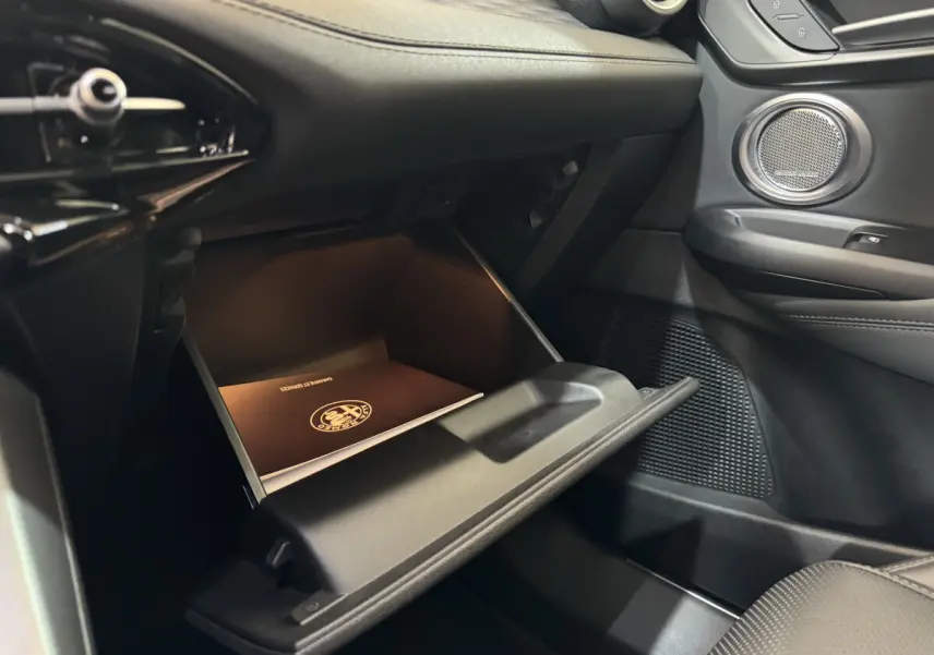 Gros plan de la boîte à gants ouverte côté passager de l'Alfa Romeo Tonale rouge avec manuel de bord visible.
