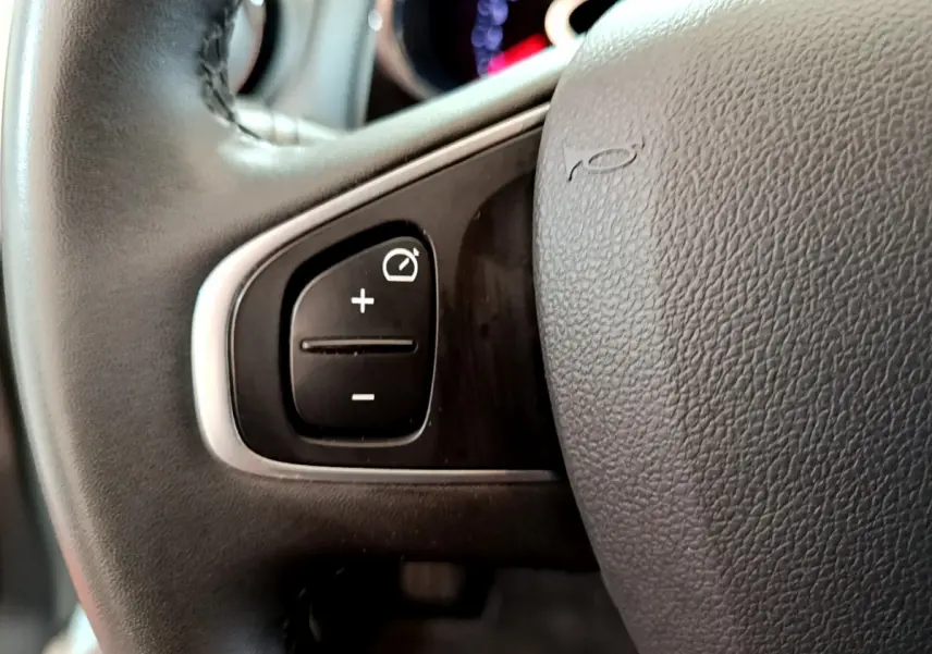 Gros plan sur les commandes du régulateur de vitesse au volant cuir noir d'une Renault Clio Business blanche de 2019.