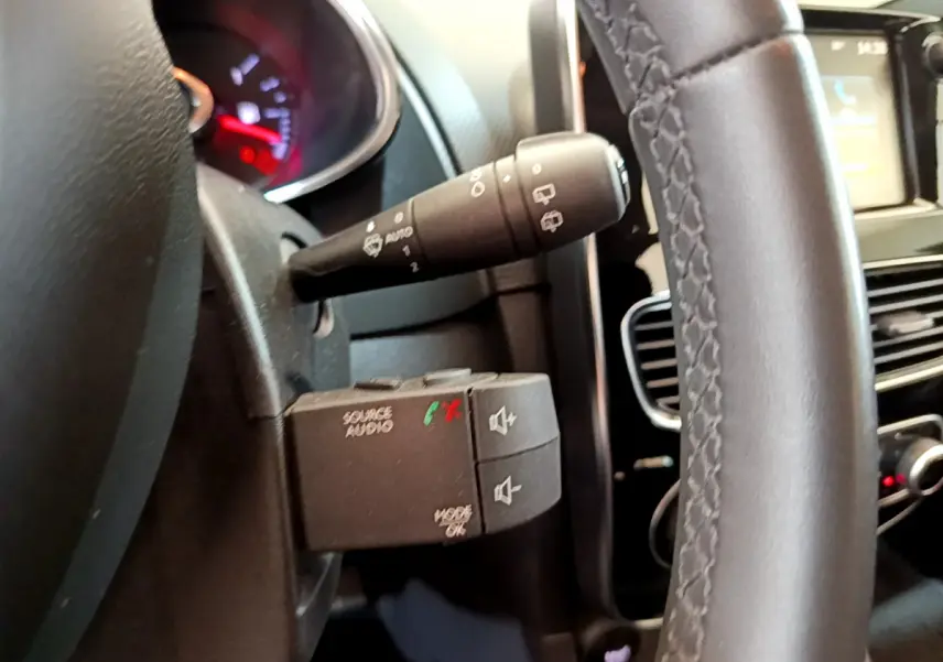 Gros plan sur la commande audio au volant cuir noir d'une Renault Clio Business TCe 90 blanche, tableau de bord en arrière-plan.