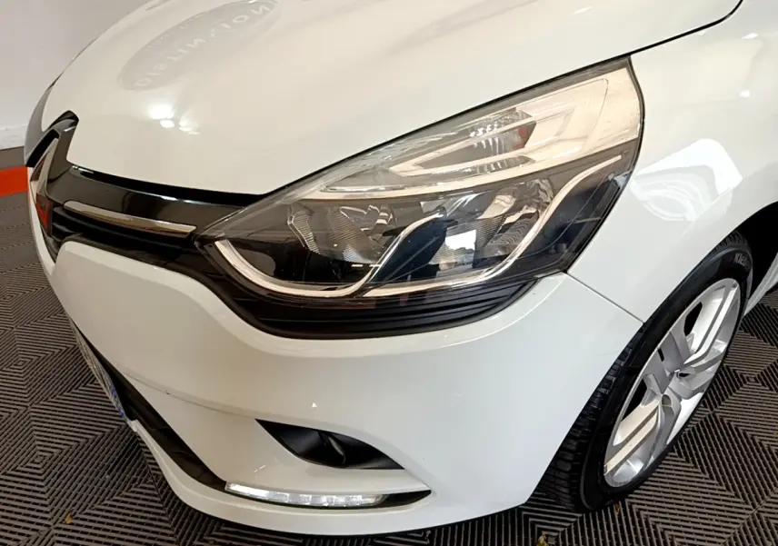 Gros plan sur l'avant droit d'une Renault Clio Business TCe 90 blanche, mettant en valeur son phare LED et la calandre noire.