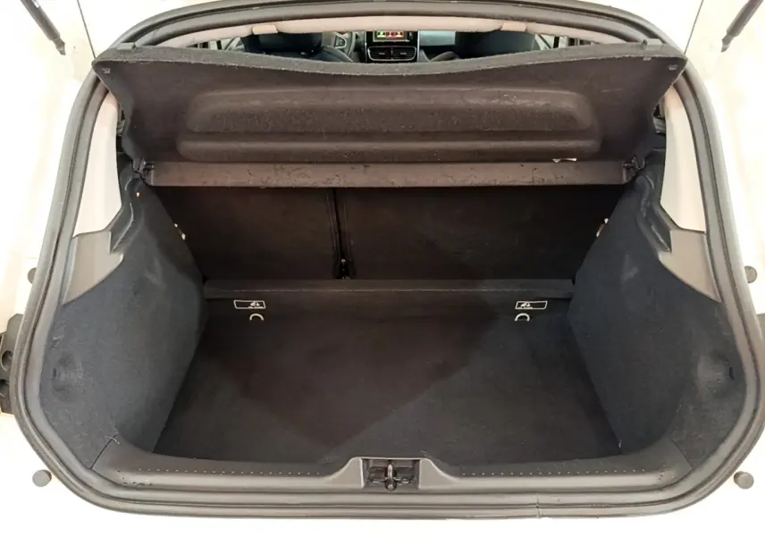 Coffre ouvert vu de l'arrière d'une Renault Clio Business blanche, intérieur noir et tablette de coffre relevée.
