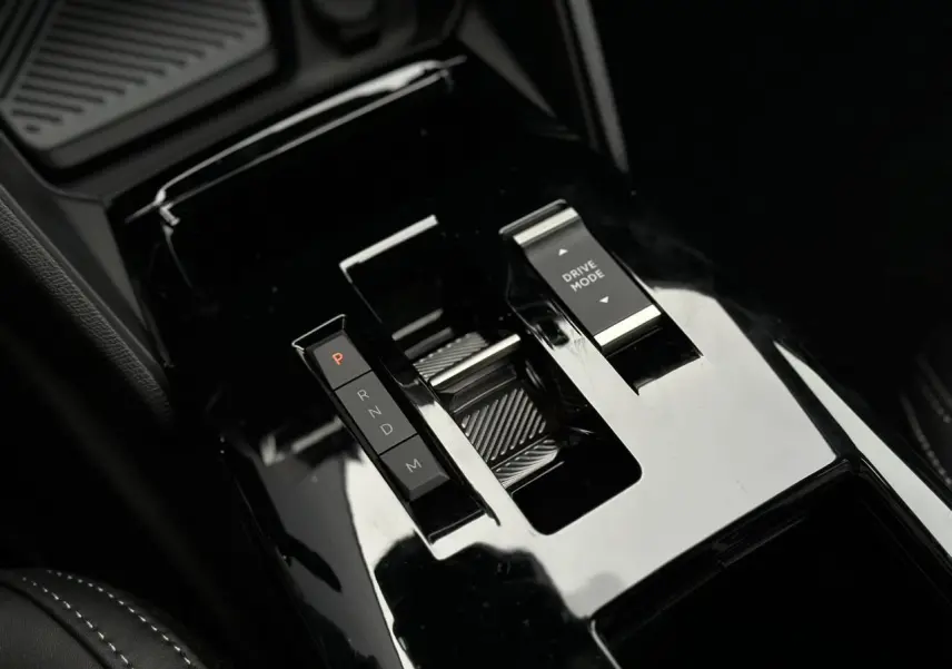 Gros plan sur la console centrale noire brillante du Citroën C4 NV Hybrid 145 e-DSC6 Max avec commandes de boîte auto et mode de conduite.