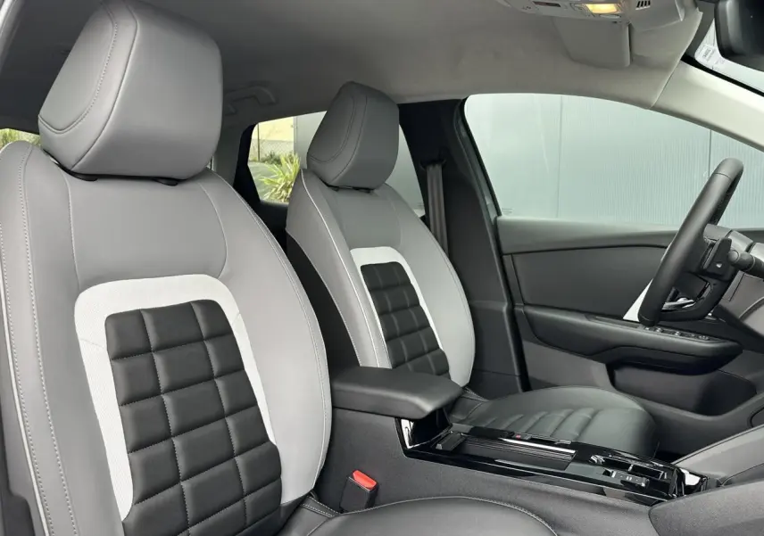 Vue intérieure côté conducteur de la Citroën C4 2025, sièges Advanced Comfort gris et noir avec accoudoir central.