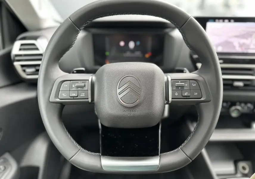 Gros plan sur le volant cuir noir de la Citroën C4 NV Hybrid 2025 avec commandes intégrées et logo central chrome.