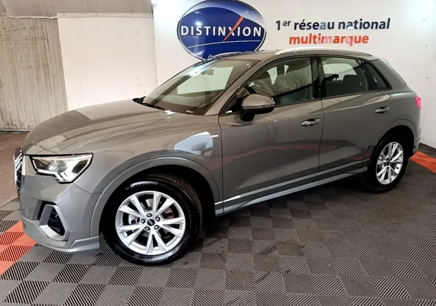Audi Q3 gris foncé vue 3/4 avant droit, avec jantes alliage et rétroviseurs assortis dans un showroom.
