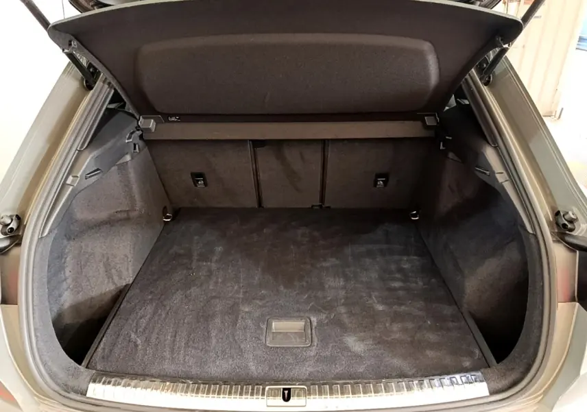 Coffre ouvert vu de l'arrière d'un Audi Q3 gris foncé, avec tapis de sol noir et habillage intérieur sombre.