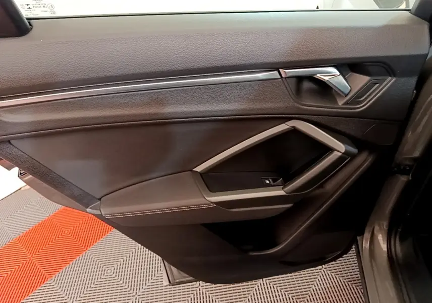 Vue intérieure du panneau de porte avant droit de l'Audi Q3 gris foncé, avec poignée chromée et accoudoir noir.