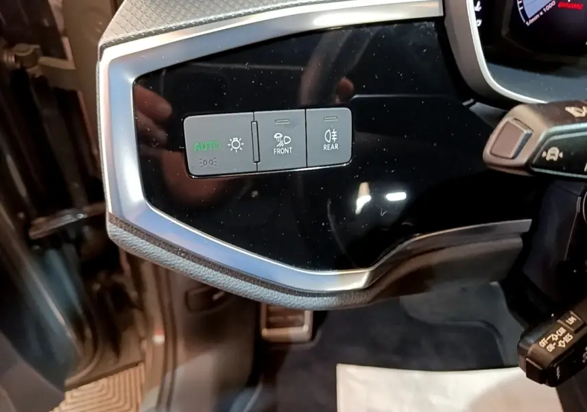 Vue rapprochée des commandes d’éclairage sur le tableau de bord noir brillant de l’Audi Q3 gris foncé.