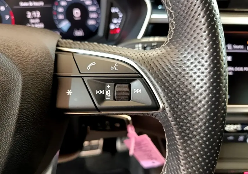 Gros plan sur le côté gauche du volant cuir perforé de l'Audi Q3 gris foncé avec commandes audio et téléphone intégrées.