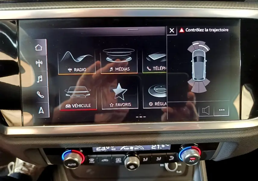 Écran tactile central affichant l'aide au stationnement et les réglages multimédias dans un Audi Q3 gris foncé.